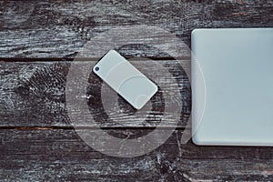 Close-up photo of a laptop and smartphone on wooden table outdoors.