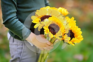 Close-up photo of little boy holding bunch of sunflowers outdoors