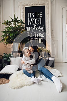 Close-up photo of little girl in knitted sweater kiss her mother while sitting on sofa at Christmas