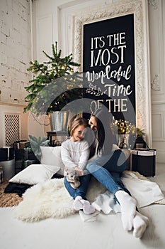 Close-up photo of little girl in knitted sweater kiss her mother while sitting on sofa at Christmas