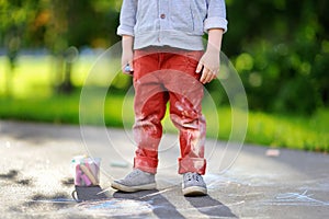 Close-up photo of little kid boy drawing with colored chalk on asphalt