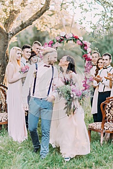 The close-up photo of the lovely wedding ceremony in the sunny wood. The smiling newlywed couple at the background of