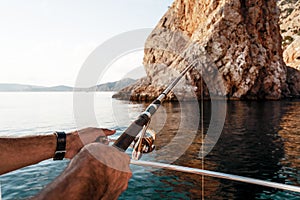 Close up of male hands holding fishing rod while fishing on sailboat in open sea