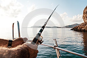 Close up of male hands holding fishing rod while fishing on sailboat in open sea