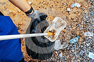 Close up photo of a man collecting garbage with a grabbing tool on the beach
