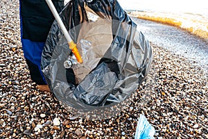 Close up photo of a man collecting garbage with a grabbing tool on the beach