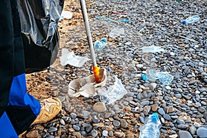 Close up photo of a man collecting garbage with a grabbing tool on the beach