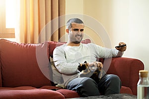 Close up photo of man holding tv remote control and relaxing with the cat.