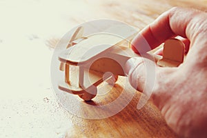 Close up photo of man's hand holding wooden toy airplane over wooden background. filtered image. aspiration and simplicity concep