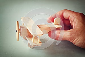 Close up photo of man's hand holding wooden toy airplane over wooden background. filtered image. aspiration and simplicity concept