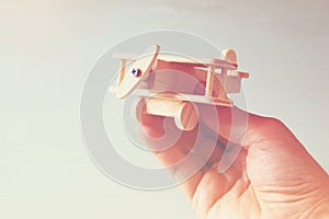 Close up photo of man's hand holding wooden toy airplane over wooden background. filtered image. aspiration and simplicity concept