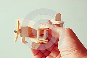 Close up photo of man's hand holding wooden toy airplane over wooden background. filtered image. aspiration and simplicity concept