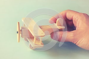 Close up photo of man's hand holding wooden toy airplane over wooden background. filtered image. aspiration and simplicity concept