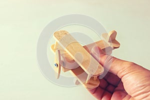 Close up photo of man's hand holding wooden toy airplane over wooden background. filtered image. aspiration and simplicity concept