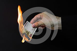 Close-up photo, a man`s hand holds an almost burnt banknote of rubles on a dark background