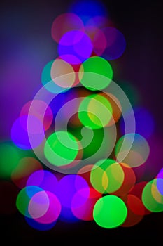 Close up photo of the multi-colored lights on the Christmas tree on dark background. The whole shot is defocused to use bokeh