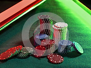 Close-up photo of a multicolored chips piles, some of them laying nearby on green cover of playing table, under green