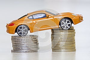 Close-up photo of new bright shiny yellow luxurious expensive toy sport car on two piles of metallic golden and silver coins as sy