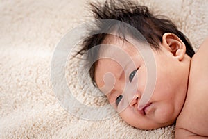 Close-up photo of newborn baby`s face girl, lying prone in the brown bed, The little girl wore pampers and lay staring at