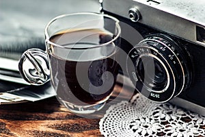 Close up photo of old, vintage camera lens with cap of coffee and black and white photos over wooden table.