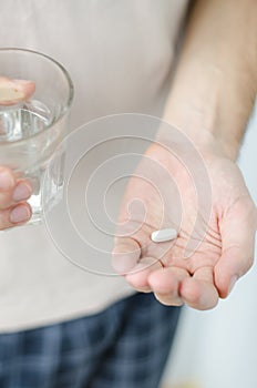 Close up photo of one round pill in young male hand. Man takes medicines with glass of water. Daily norm of vitamins, effective dr