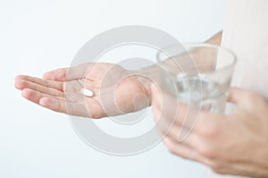 Close up photo of one round pill in young male hand. Man takes medicines with glass of water. Daily norm of vitamins, effective dr