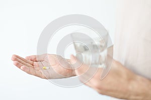 Close up photo of one round pill in young male hand. Man takes medicines with glass of water. Daily norm of vitamins, effective dr