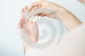 Close up photo of one round pill in young male hand. Man takes medicines with glass of water. Daily norm of vitamins, effective dr