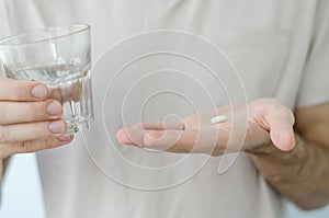 Close up photo of one round pill in young male hand. Man takes medicines with glass of water. Daily norm of vitamins, effective dr