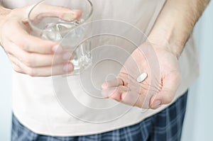 Close up photo of one round pill in young male hand. Man takes medicines with glass of water. Daily norm of vitamins, effective dr