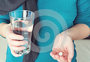 Close up photo of one round white pill in young female hand. Woman takes medicines with glass of water.