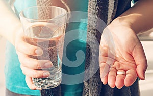 Close up photo of one round white pill in young female hand. Woman takes medicines with glass of water.