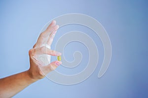 Close up photo of one round yellow pill in hand. Man takes medicines with glass of water. Daily norm of vitamins, effective drugs,