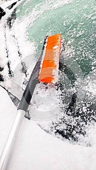 Close up photo of orange brush lying on the snow covered windshield