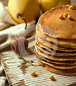 Close-up photo of a pile of fluffy buttermilk pancakes on a bright wooden surface, with a pair of pears in the distance, sea