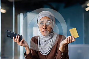 Close up photo. Portrait of a young Arab woman sitting in the office and holding a credit card in her hands. Problems