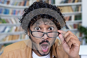 Close-up photo. Portrait of a young hispanic man in a library, bookstore, who looks at the camera in surprise, lowers
