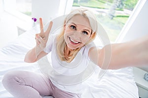 Close up photo of pretty retired house wife lady comfy bed showing v-sign symbol taking selfies stay home bedroom