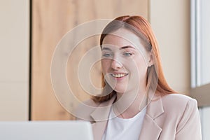 Close-up photo of a red haired business woman smiling while sitting at a computer, got a satisfactory result