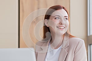 Close-up photo of a red haired business woman smiling while sitting at a computer, got a satisfactory result