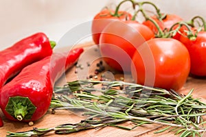 Close-up photo of red hot peppers, tomatoes with pepper peas and rosemary at the cutting board.