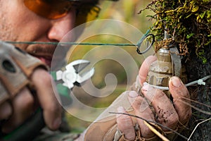 Close-up photo - a sapper clears a booby trap. The wire cutters cutting the wire of the frag grenade trap.