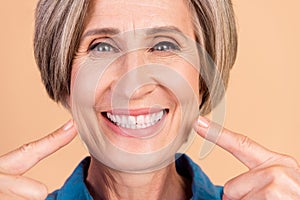 Close up photo of satisfied pensioner person with white gray hairdo directing at white healthy teeth isolated on beige