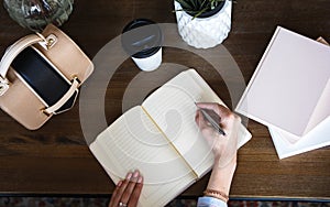 Close-up photo of scheduler notebook on a wooden table. Female hand writes on paper.