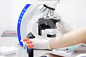 Close-up photo of scientist hands with microscope, examining samples and liquid