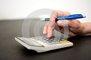 Close-up photo of senior woman's hand using calculator and pen to calculate tax