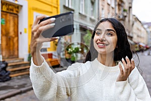 Close-up photo of a smiling young Indian girl walking on a city street, taking a selfie and talking on a video call on