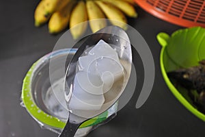 Close up photo of a spon of sweet jelly drink with a hand of banana in the background