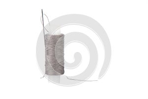 Close-up photo of a spool with gray thread and a needle isolated over white background
