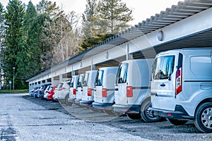 Close up photo at straight row of white colored cars and vans at parking place with roof protections from the Sun and rain, snow.